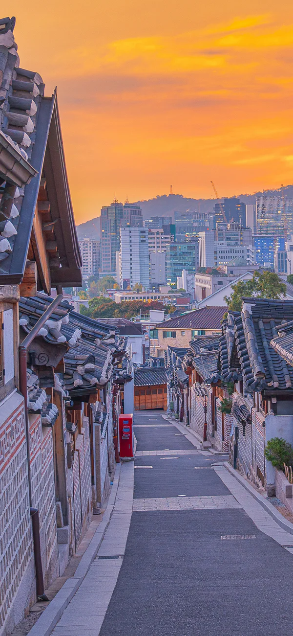 Solnedgang over Bukchon Hanok Village i Seoul, Sør-Korea, med byens skyline i bakgrunnen