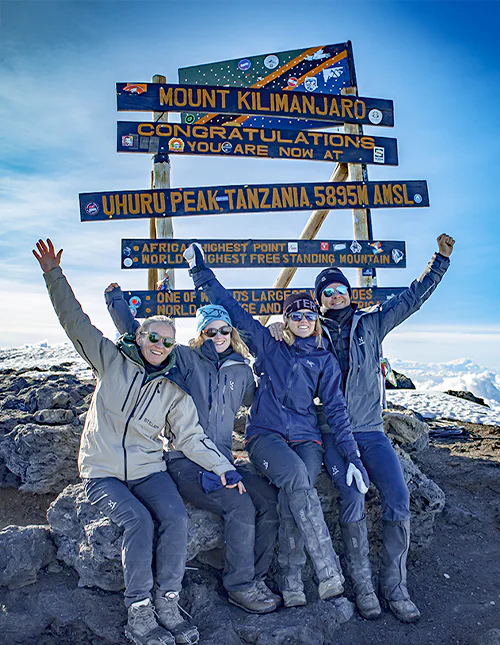 Familie sitter foran skiltet ved Uhuru Peak på toppen av Kilimanjaro