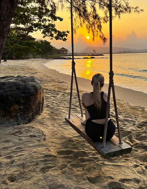 En person sitter på en huske på en strand og nyter solnedgangen