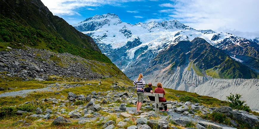 En familie på tre ser på fjellene fra utsiktspunktet Kea Point i Mount Cook nasjonalpark