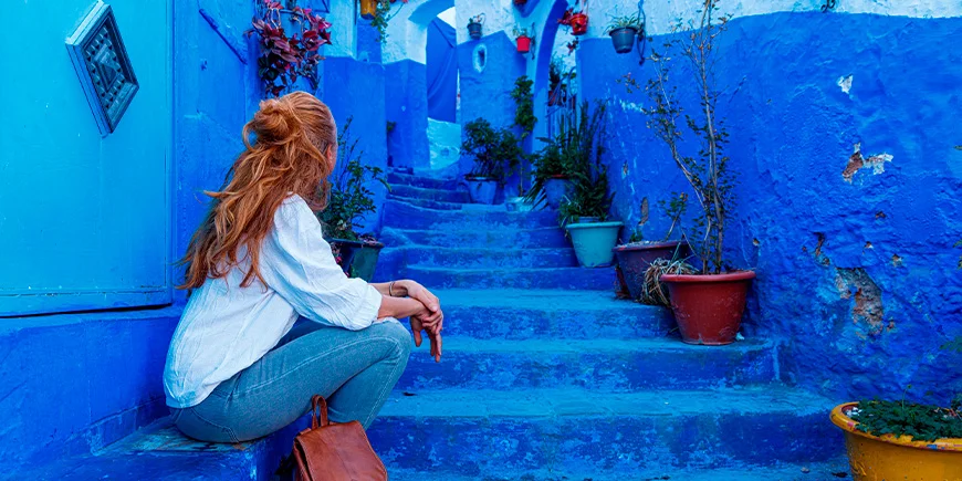 Kvinne sittende på trappen i den blå byen Chefchaouen, Marokko