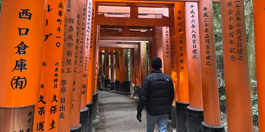 Mann går gjennom torii-portene ved Fushimi Inari