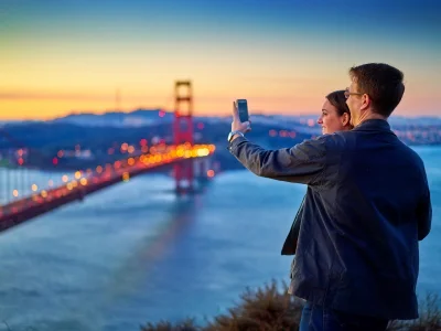 Mann og kvinne tar bilde av Golden Gate Bridge ved solnedgang