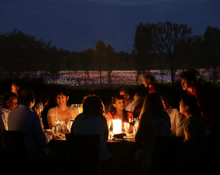 Field of Light Dinner ved Uluru i Australia med gjester rundt et middagsbord og fargerike lys i bakgrunnen