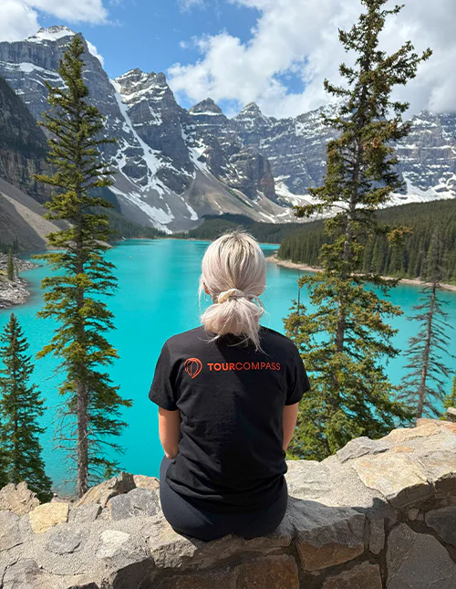Kvinne med TourCompass T-skjorte ser utover en turkisblå innsjø og snøkledde fjell i Canada