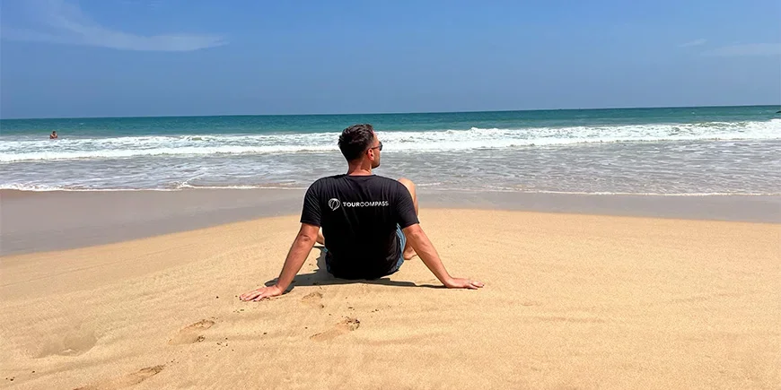Mann i TourCompass T-skjorte sitter på stranden i Mirissa på Sri Lanka
