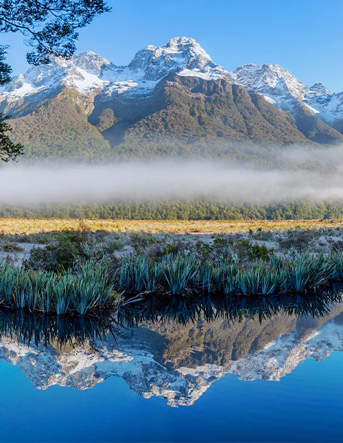 Mirror Lake, lavthengende tåke og snøkledde tinder på en klar vinterdag i Milford Sound, New Zealand