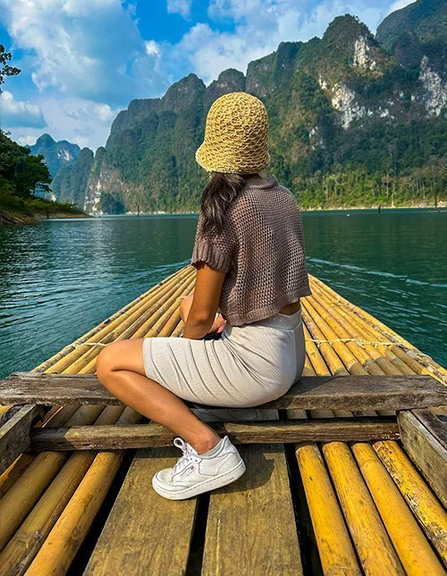 Kvinne seiler på bambusflåte på en innsjø i Thailand, omgitt av dramatiske kalksteinsfjell.