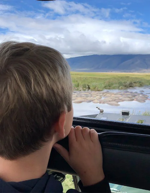 Et barn ser ut av en safaribil mot en elv og savannen
