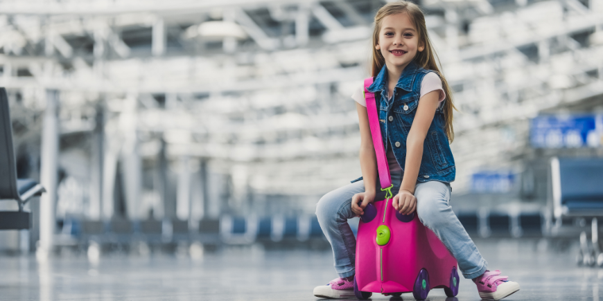 Barn sitter på en koffert på en flyplass
