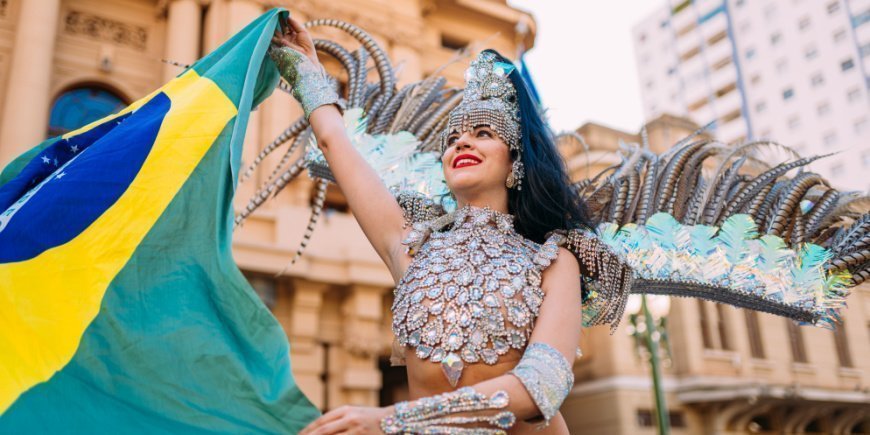 Brasiliansk kvinne iført fargerikt kostyme holder brasiliansk flagg 