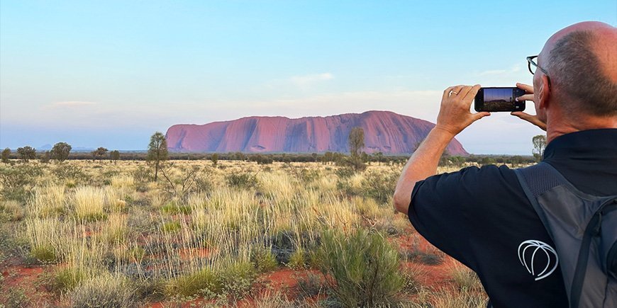 En mann tar mobilbilde av Uluru i Australia