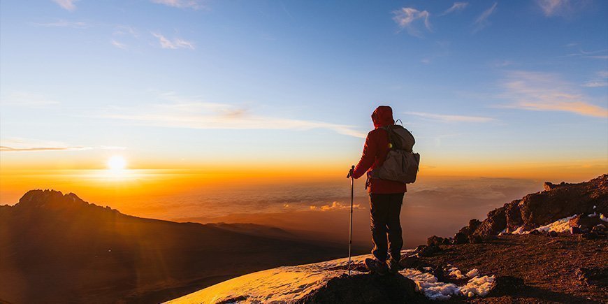 Mann står på Kilimanjaro ved soloppgang