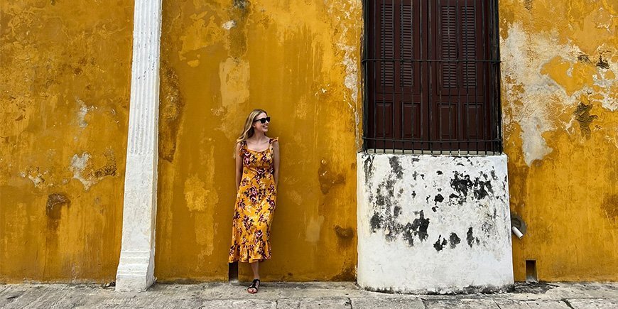Kvinne i oransje kjole lener seg mot oransje vegg i Izamal, Mexico.