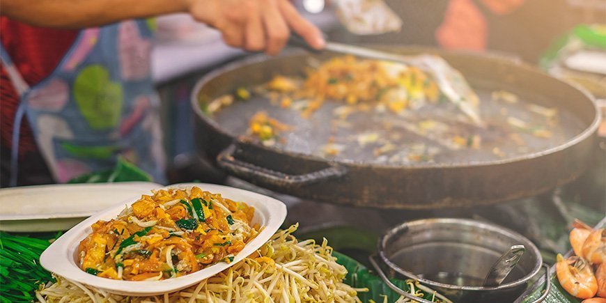 Kvinne lager Pad Thai på et marked i Bangkok