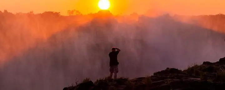 Mann tar bilder av Victoria Falls i skumringen